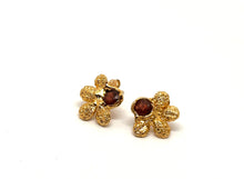 Load image into Gallery viewer, Handcrafted gold-tone stud earrings featuring a textured floral design used Japanese Pieris plant, with a deep red garnet gemstone at the center – artisan jewelry by Floweredsky Designs